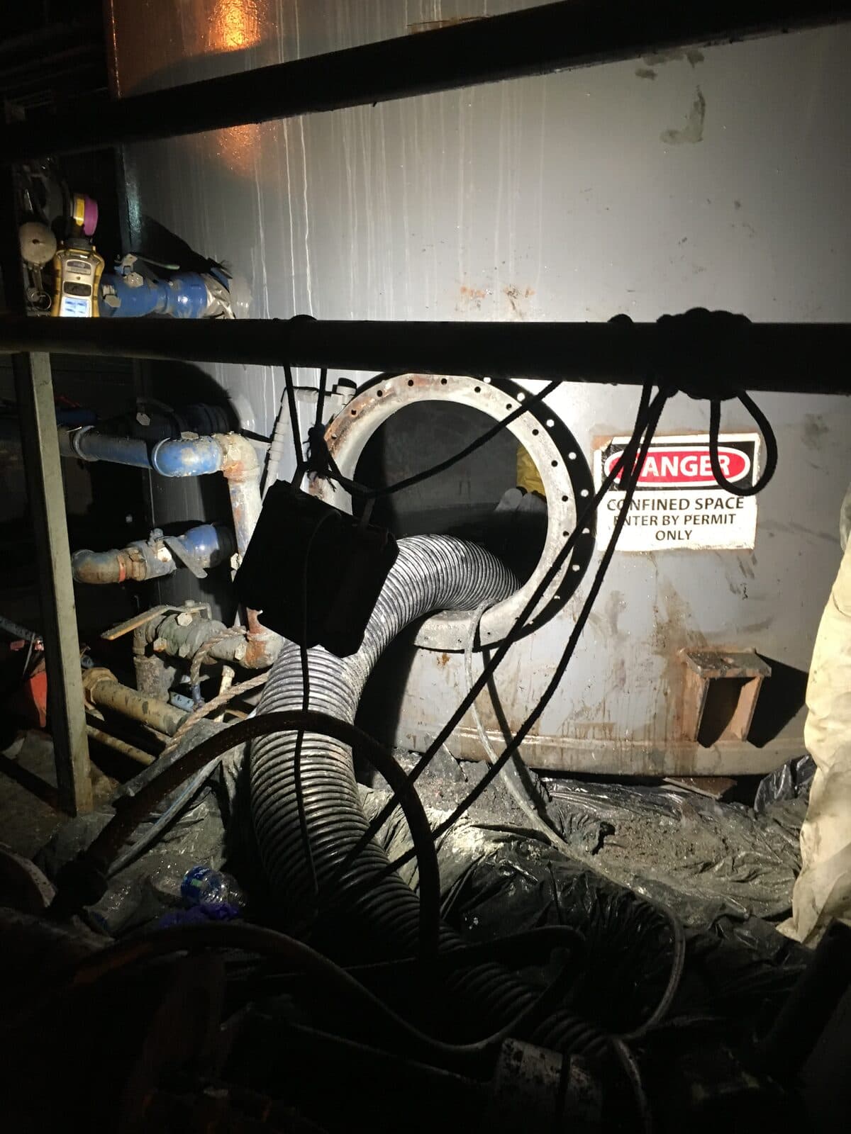 Vacuum hoses rigged to a confined-space manway with gas monitor for line cleaning