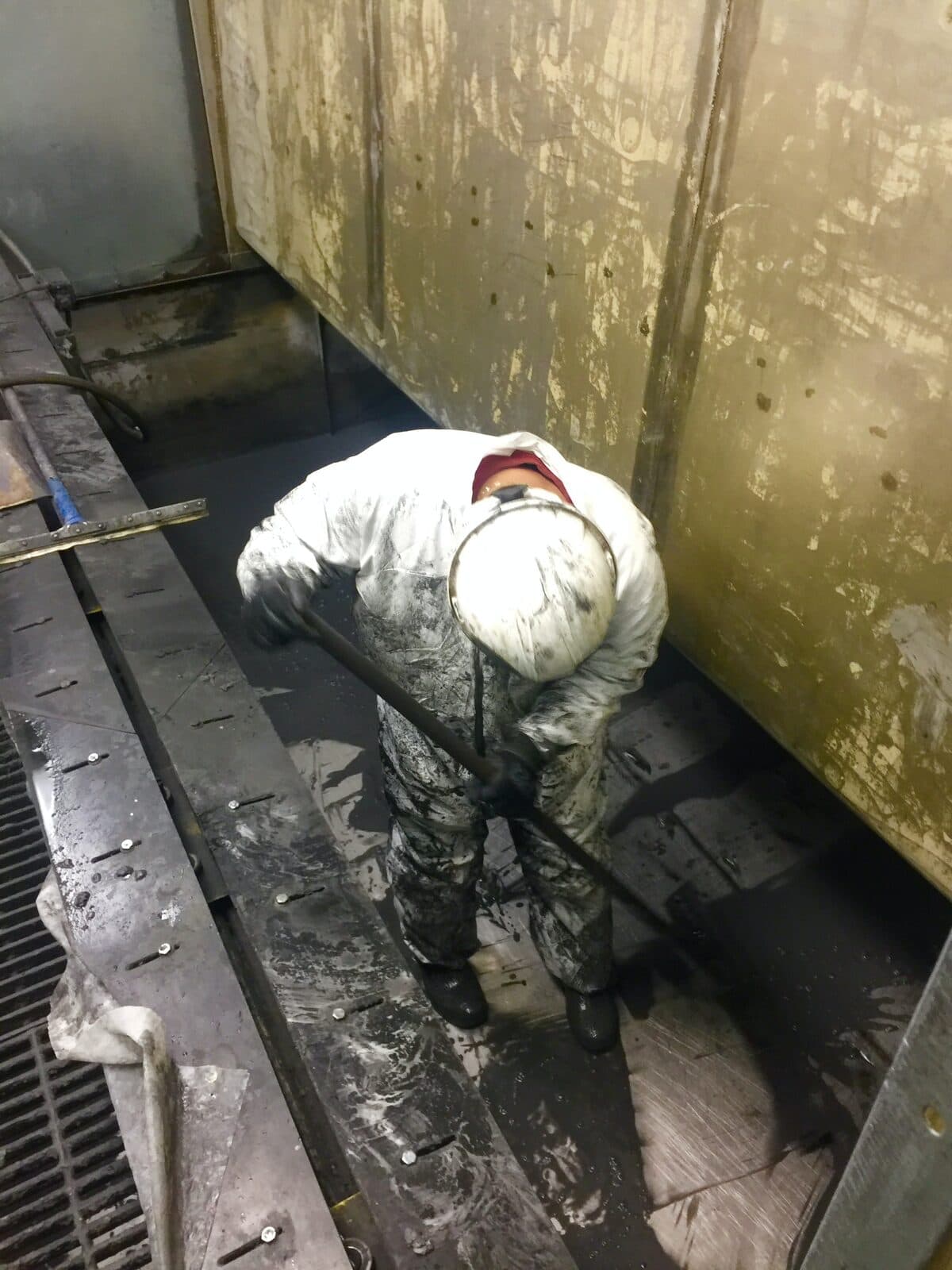 Technician in a full suit shoveling sludge inside a confined vessel